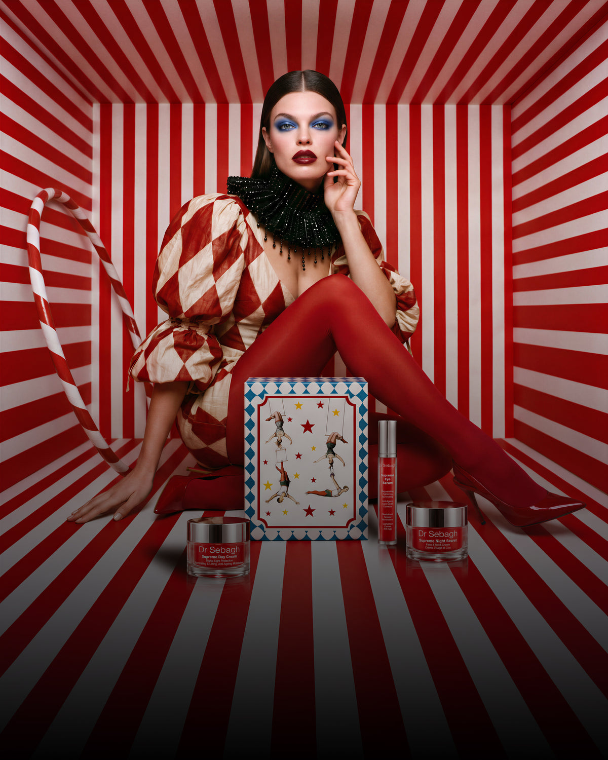 Dr Sebagh vintage circus Christmas gift box lid held by a model in a red and white harlequin costume, with Supreme skincare