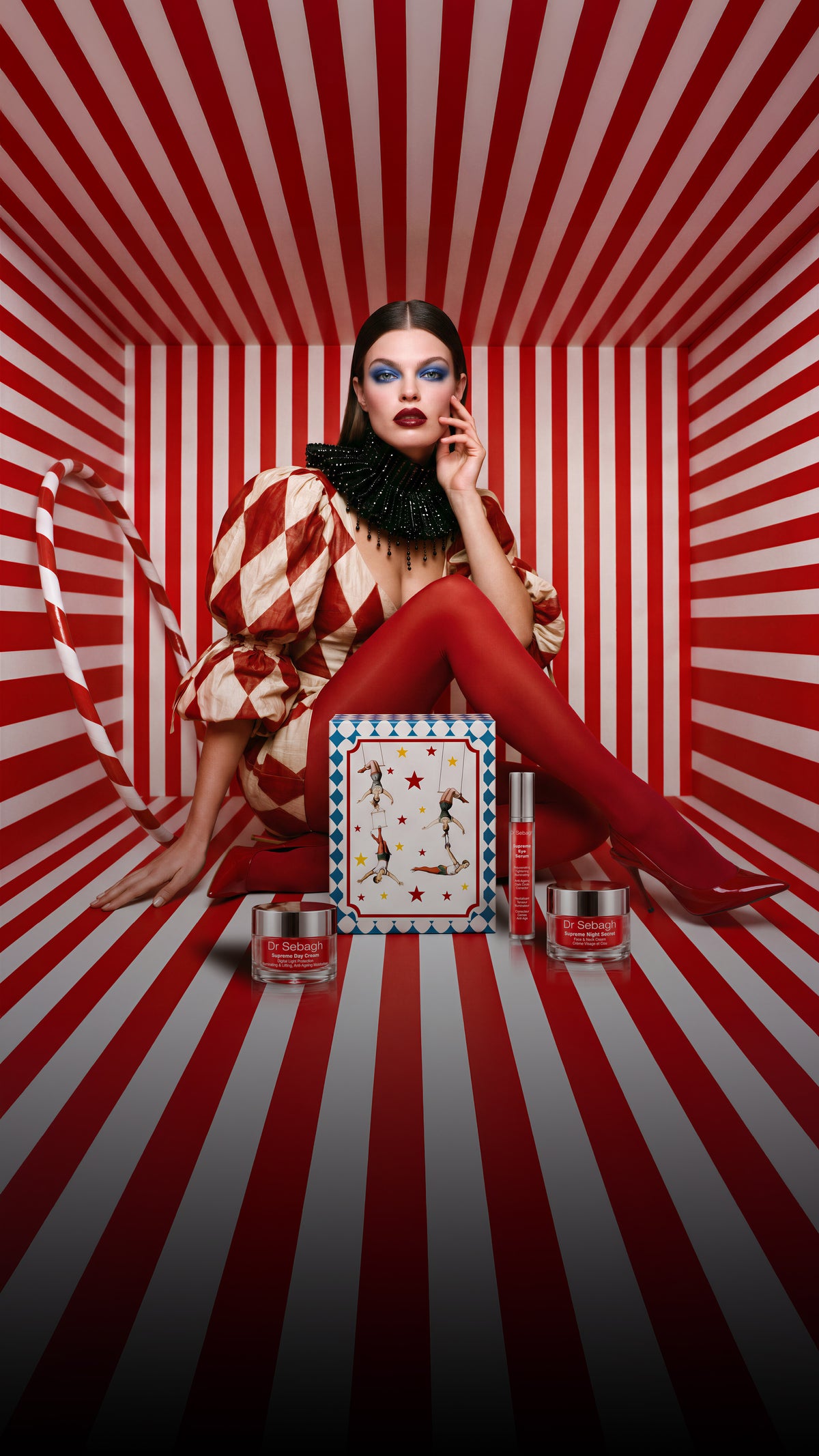 Dr Sebagh vintage circus Christmas gift box lid held by a model in a red and white harlequin costume, with Supreme skincare