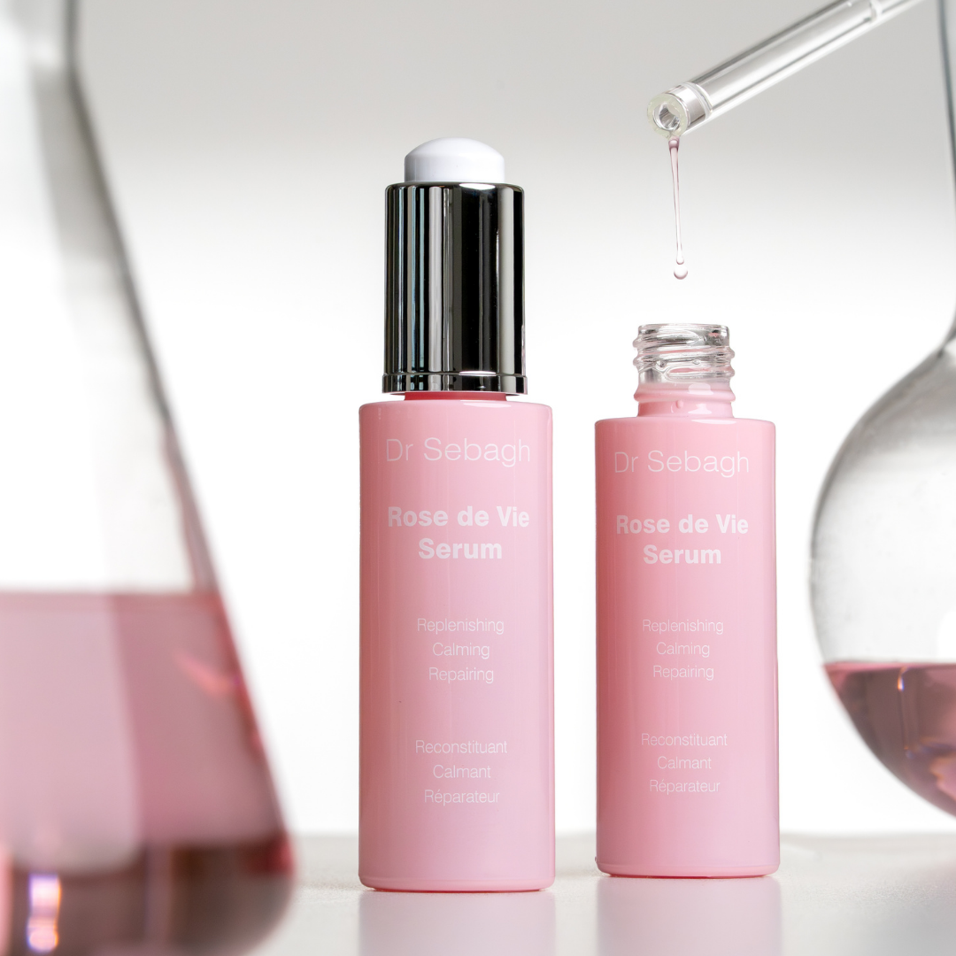 Two pink bottles of Dr Sebagh Rose de Vie Serum with a dropper on a reflective surface.