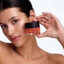 Model holding Dr Sebagh Deep Exfoliating Mask jar beside her cheek