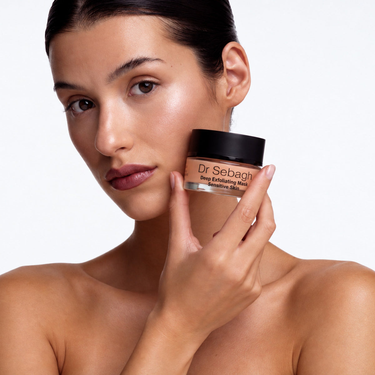 Model holding Dr Sebagh Deep Exfoliating Mask Sensitive Skin jar against her jaw